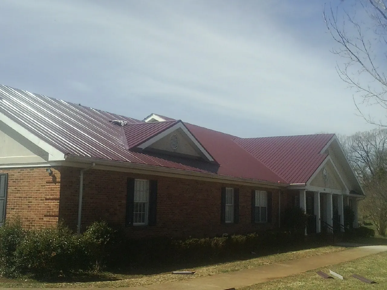 Red metal roof with gabled entries on a long brick building, from a Hail Damage Roof Repair job in Hookstown