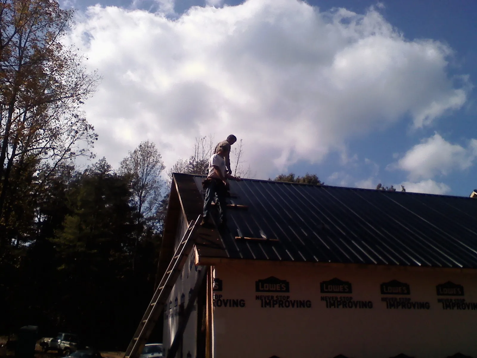 Roofer fastening dark metal panels high against a cloudy sky, from a Roof Inspection job in Hookstown