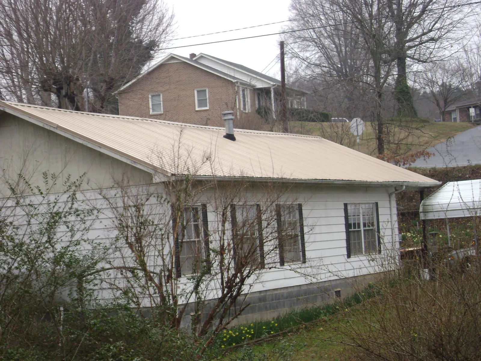 Tan metal roof on a white sided house set into a hillside — Commercial Roofing by Roofing Brothers in Hookstown